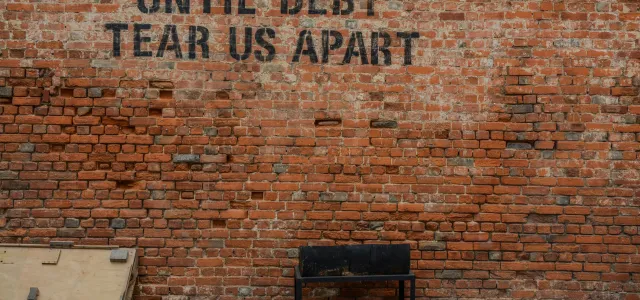 Until debt tear us apart printed red brick wall at daytime by Alice Pasqual courtesy of Unsplash.