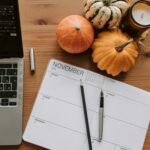 Cozy autumn workspace featuring a notebook, pumpkins, and a laptop on a wooden table.