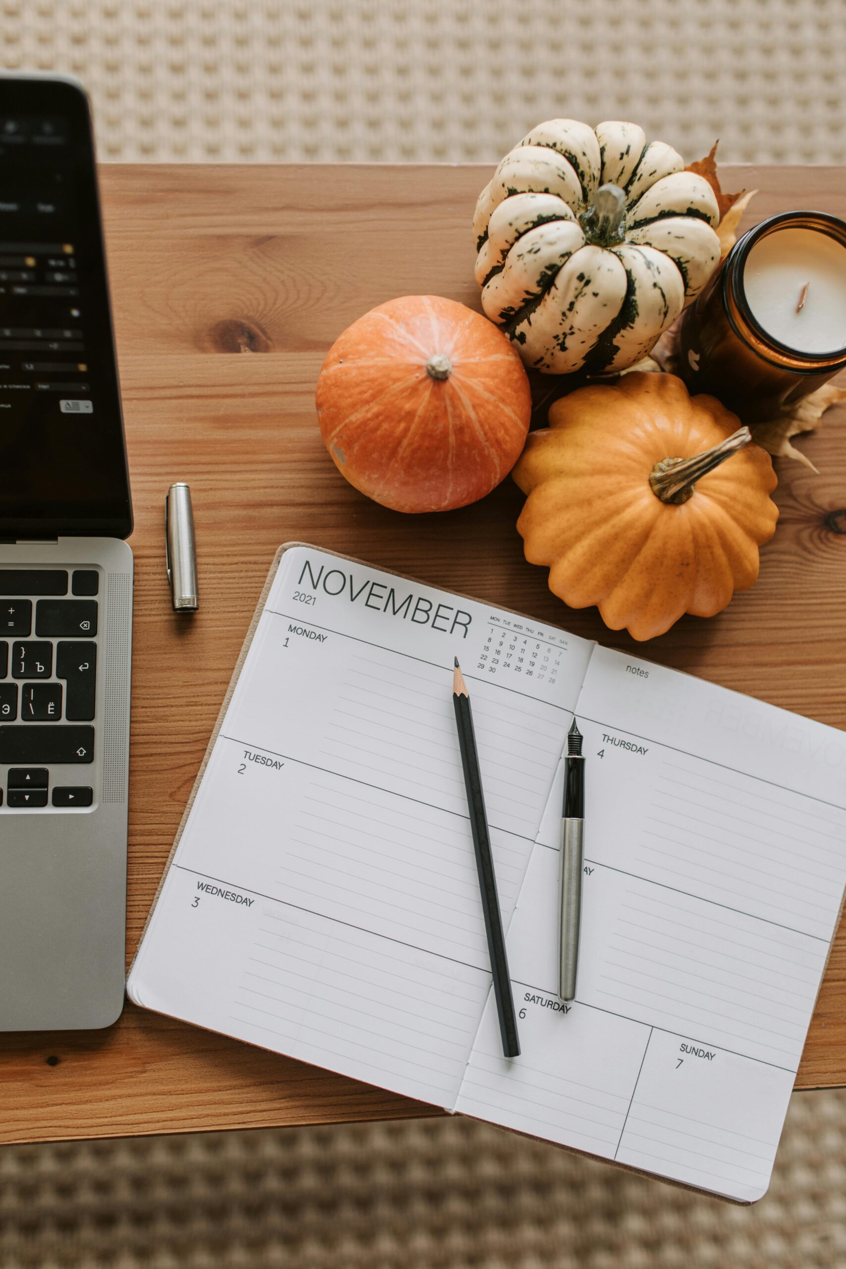 Cozy autumn workspace featuring a notebook, pumpkins, and a laptop on a wooden table.